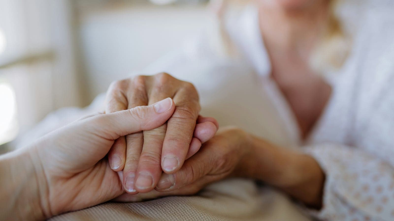 A younger hand holding an older hand in a hospital setting
