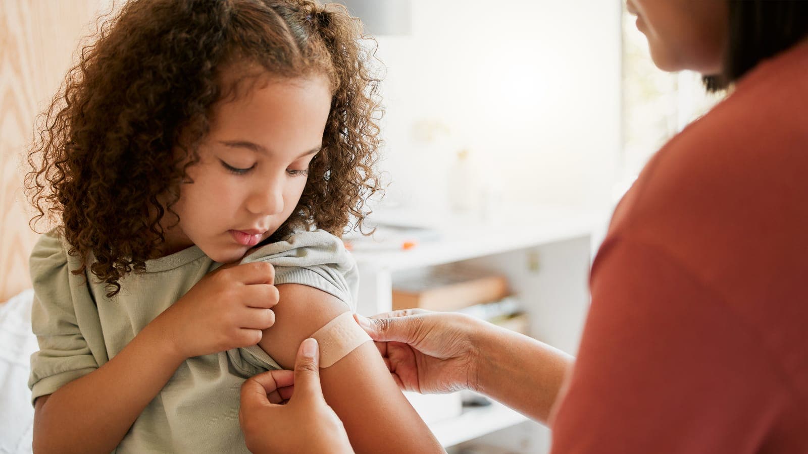 A healthcare worker puts a bandage on a little girl's arm after a vaccination
